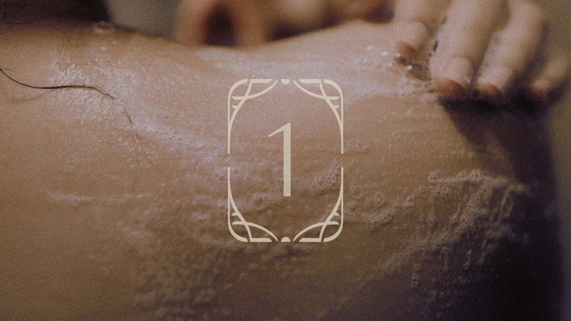 The Belantara Logo monogram containing a big number 1 shown over the picture of a woman gently lathering her back.