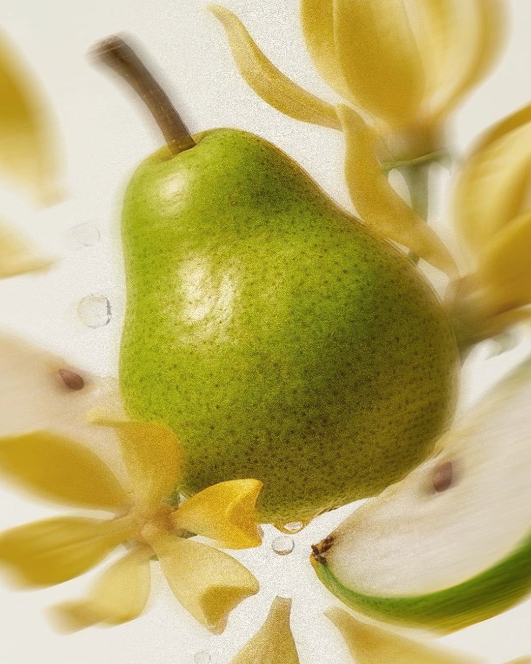 Green pear surrounded by yellow ylang ylang flowers on a light background.