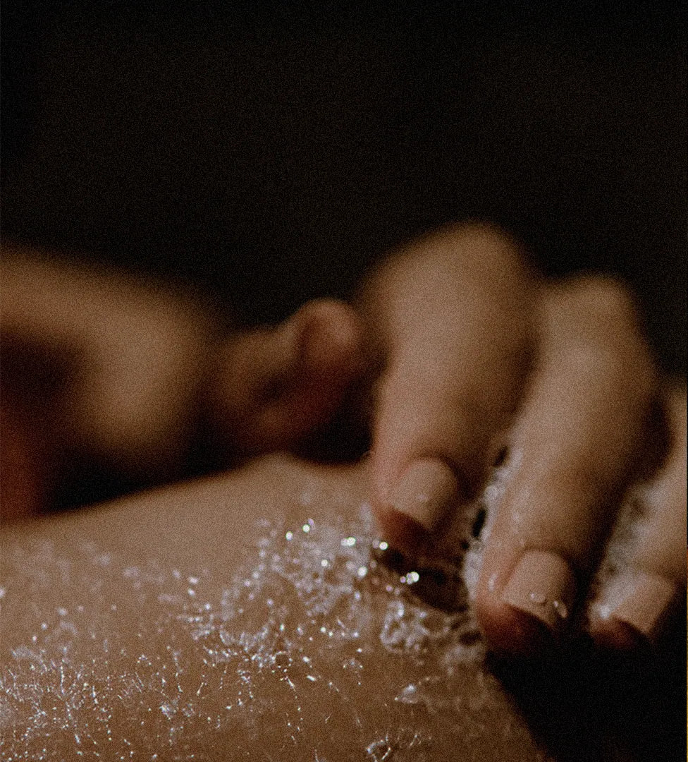 Close-up of a hand applying cleanser to their own skin over a dark background.