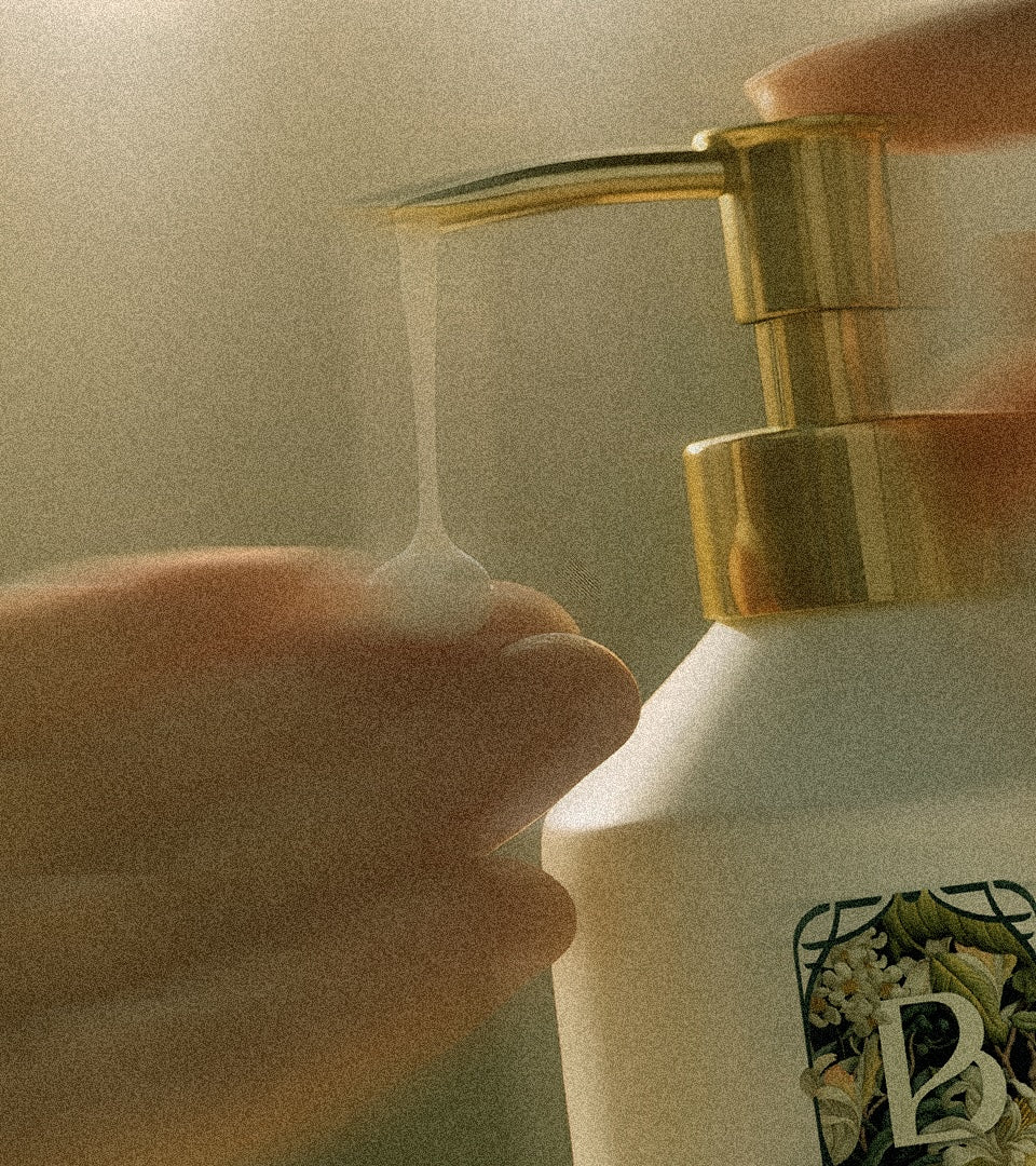 Hand pressing a gold pump on a bottle of Belantara Mango Butter Hand & Body Lotion with a brand logo.