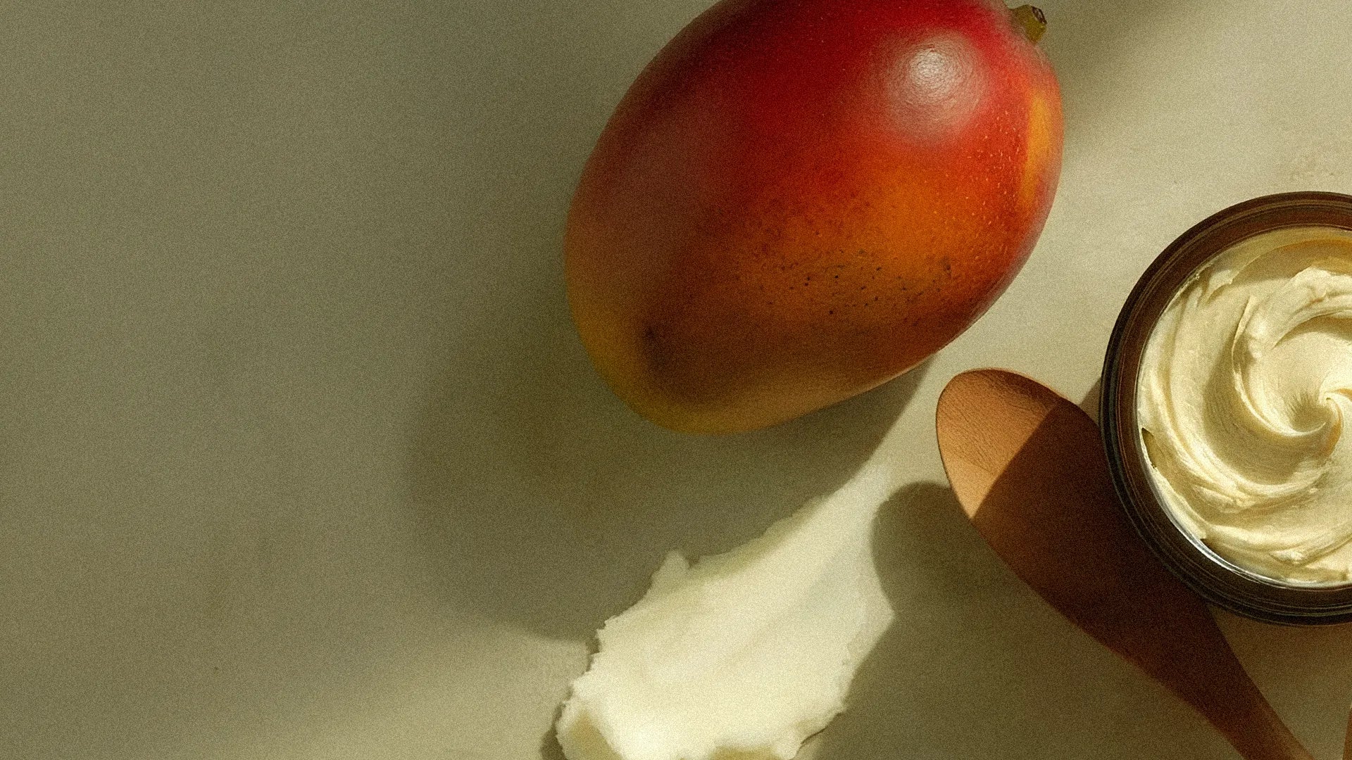 Mango and a container of mango butter on a neutral background