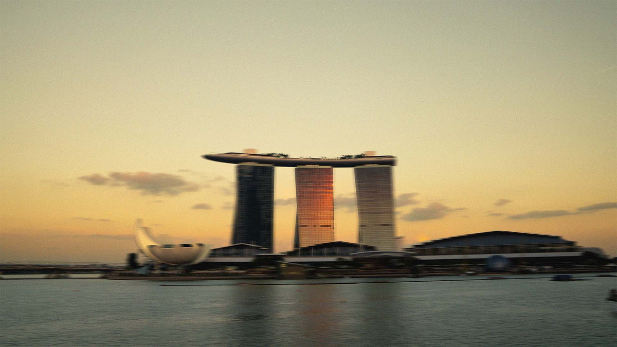 A scenic view of Marina Bay Sands in Singapore at sunset, with the three towers and the sky park bridge reflected in the calm water.