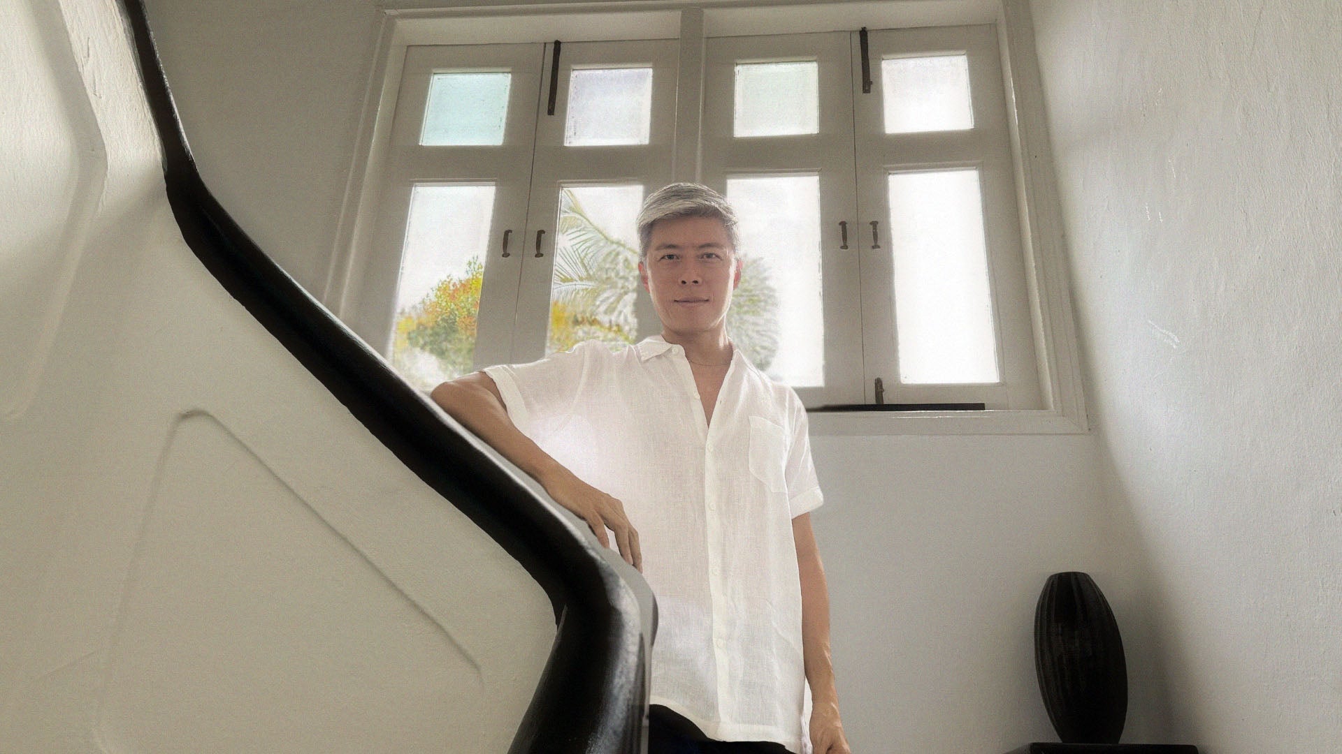 Shawn, the CEO and co-founder of Belantara, stands in the staircase of a colonial black and white bungalow in Singapore.