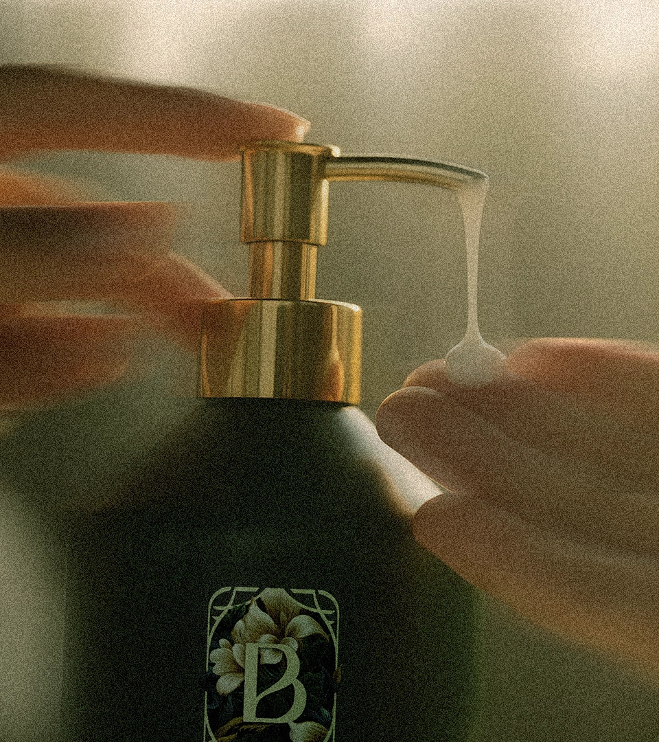 Hand pressing a gold pump on a bottle of Belantara Mango Butter Hand & Body Wash with a brand logo.