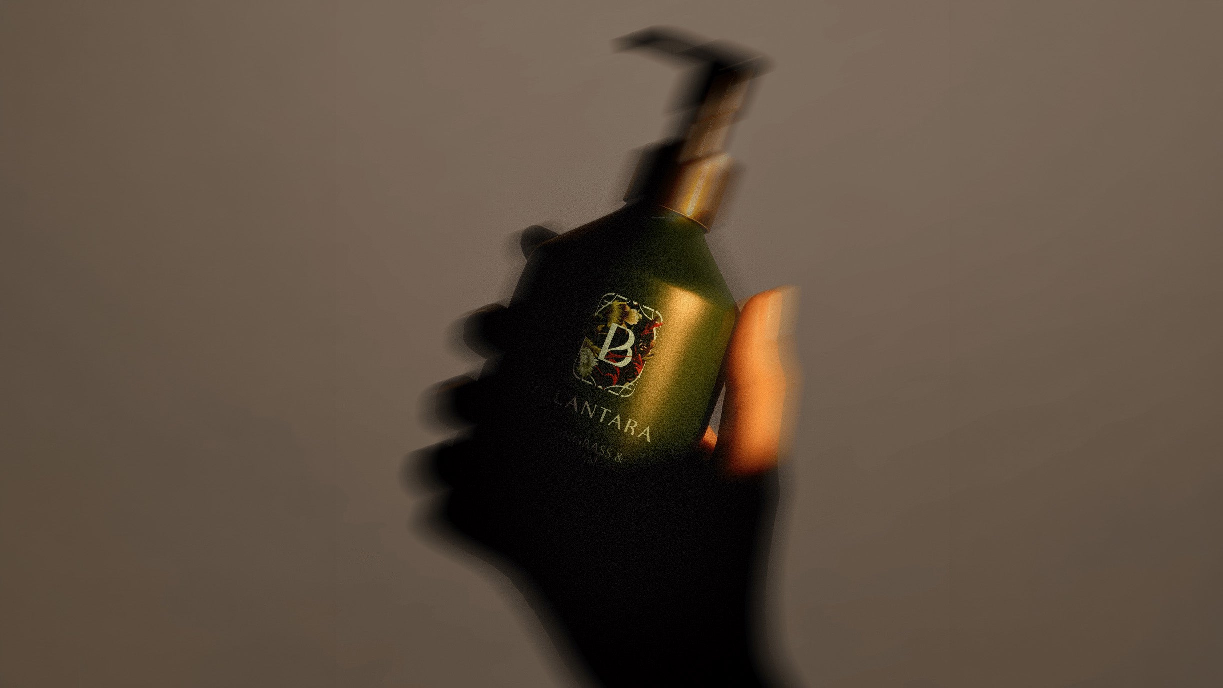 Hand holding a Belantara Hand & Body Wash bottle with a logo against a gray background.