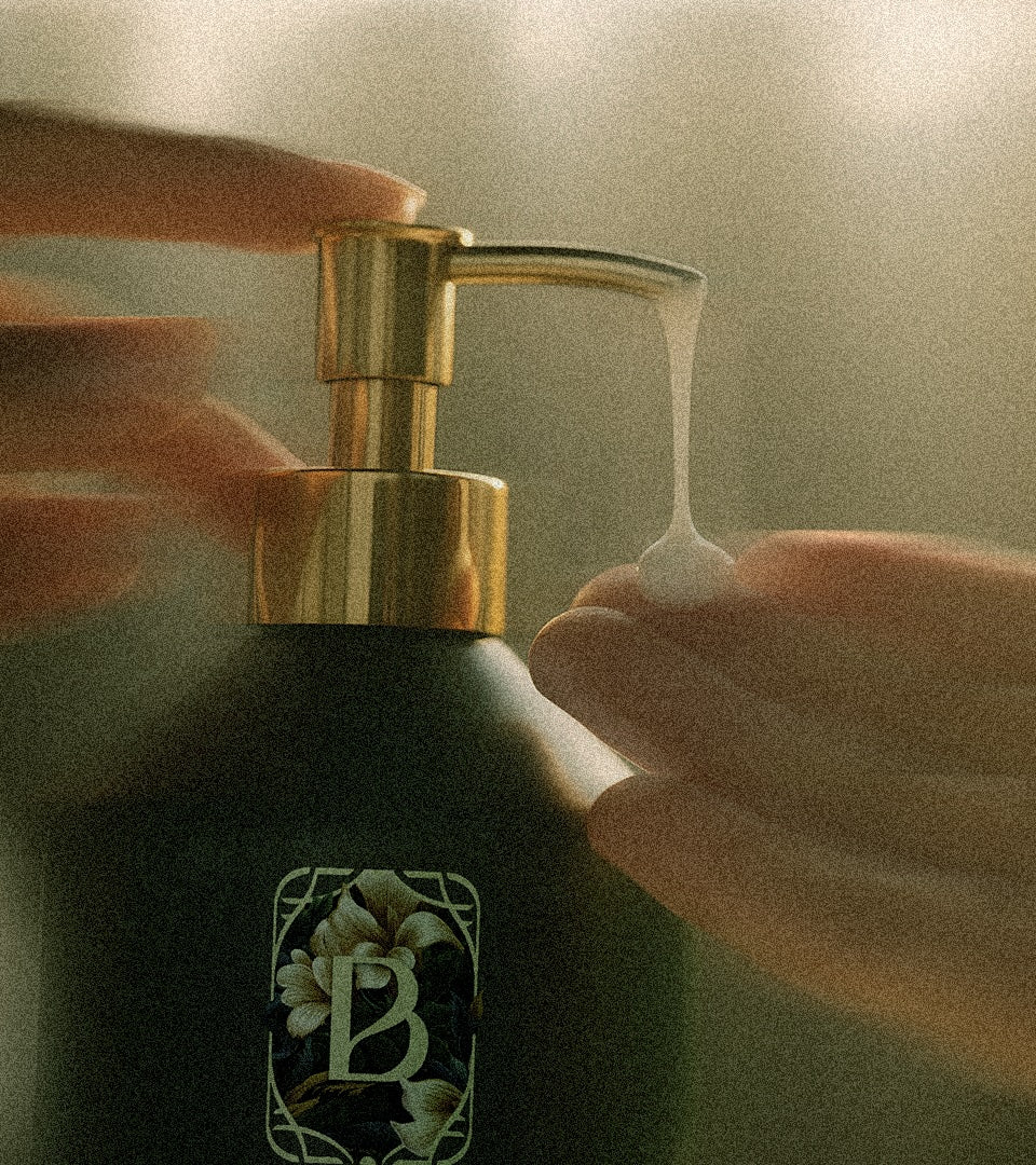 Hand pressing a gold pump on a bottle of Belantara Mango Butter Hand & Body Wash with a brand logo.