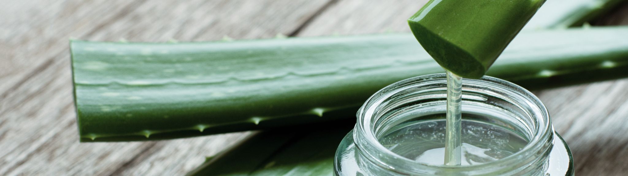 A glass jar being filled with aloe vera extract from an aloe plant leaf on a wooden surface.
