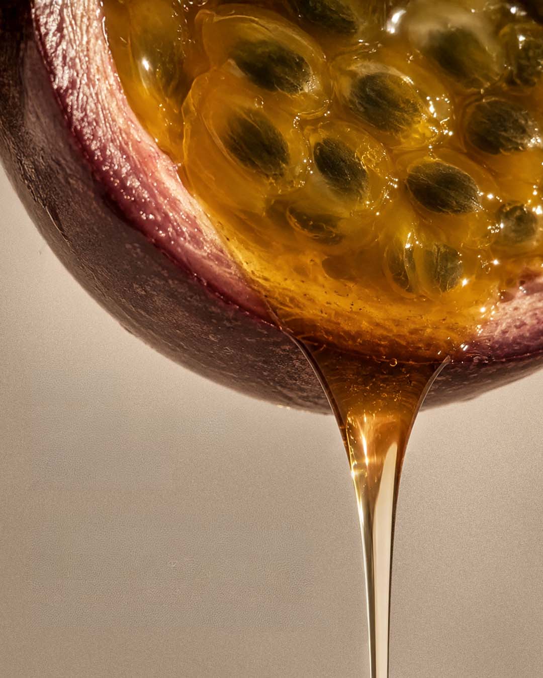 Close-up of a halved passion fruit with seeds and juice on a neutral background.