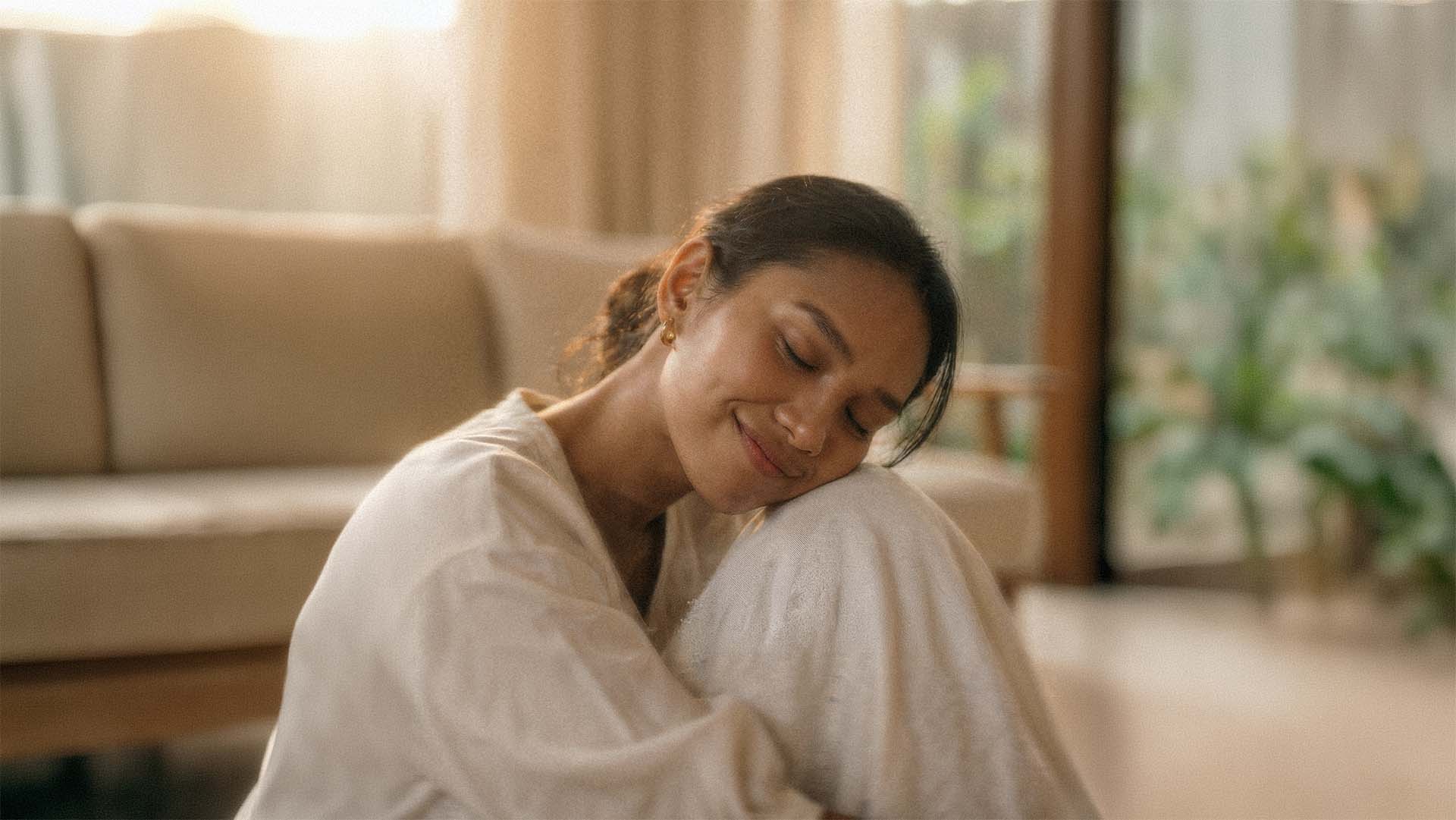 Woman with a gentle smile feeling comforted while sitting in a cozy living room with a warm ambiance.
