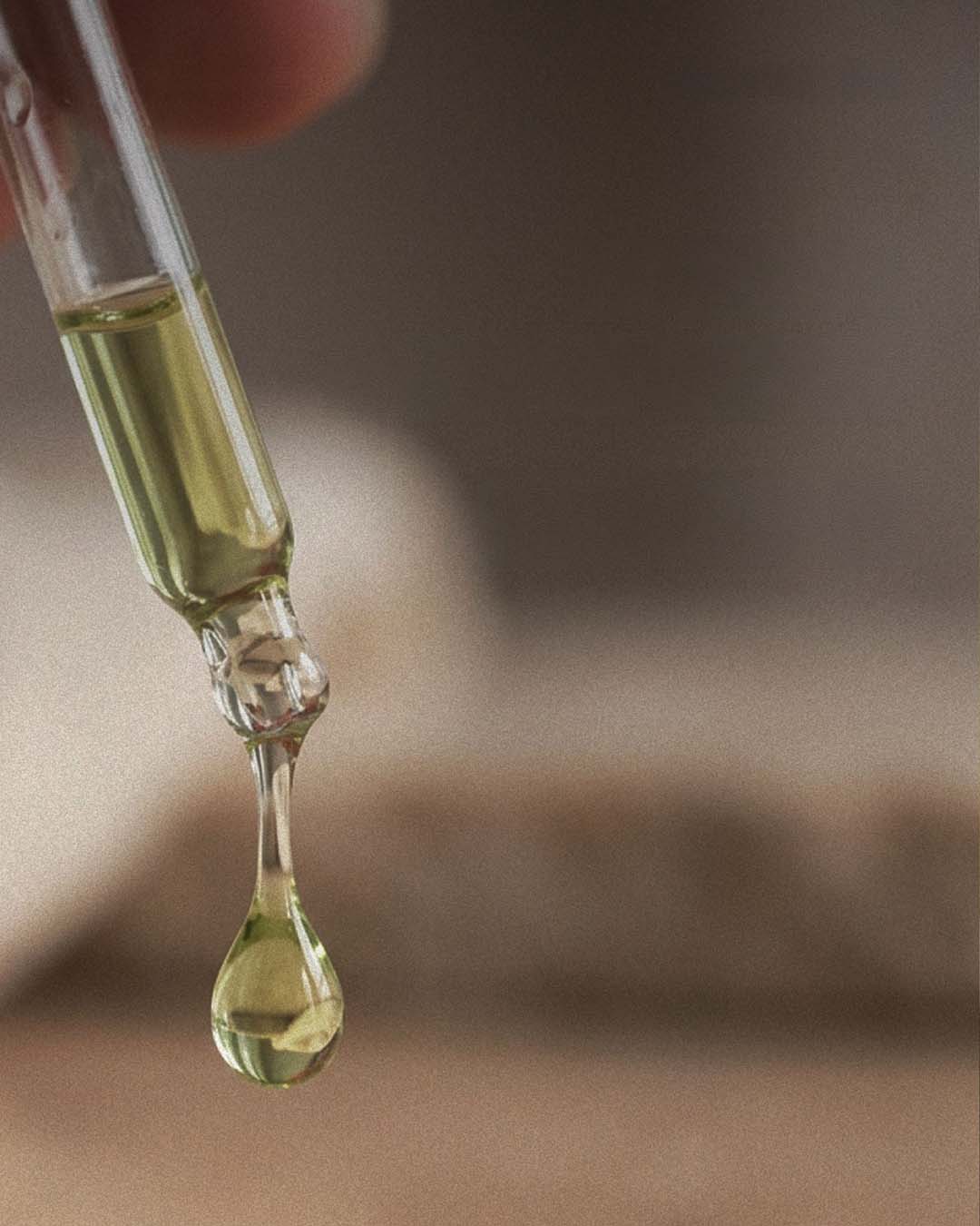 Close-up of a dropper with a drop of tamanu oil on a blurred background.